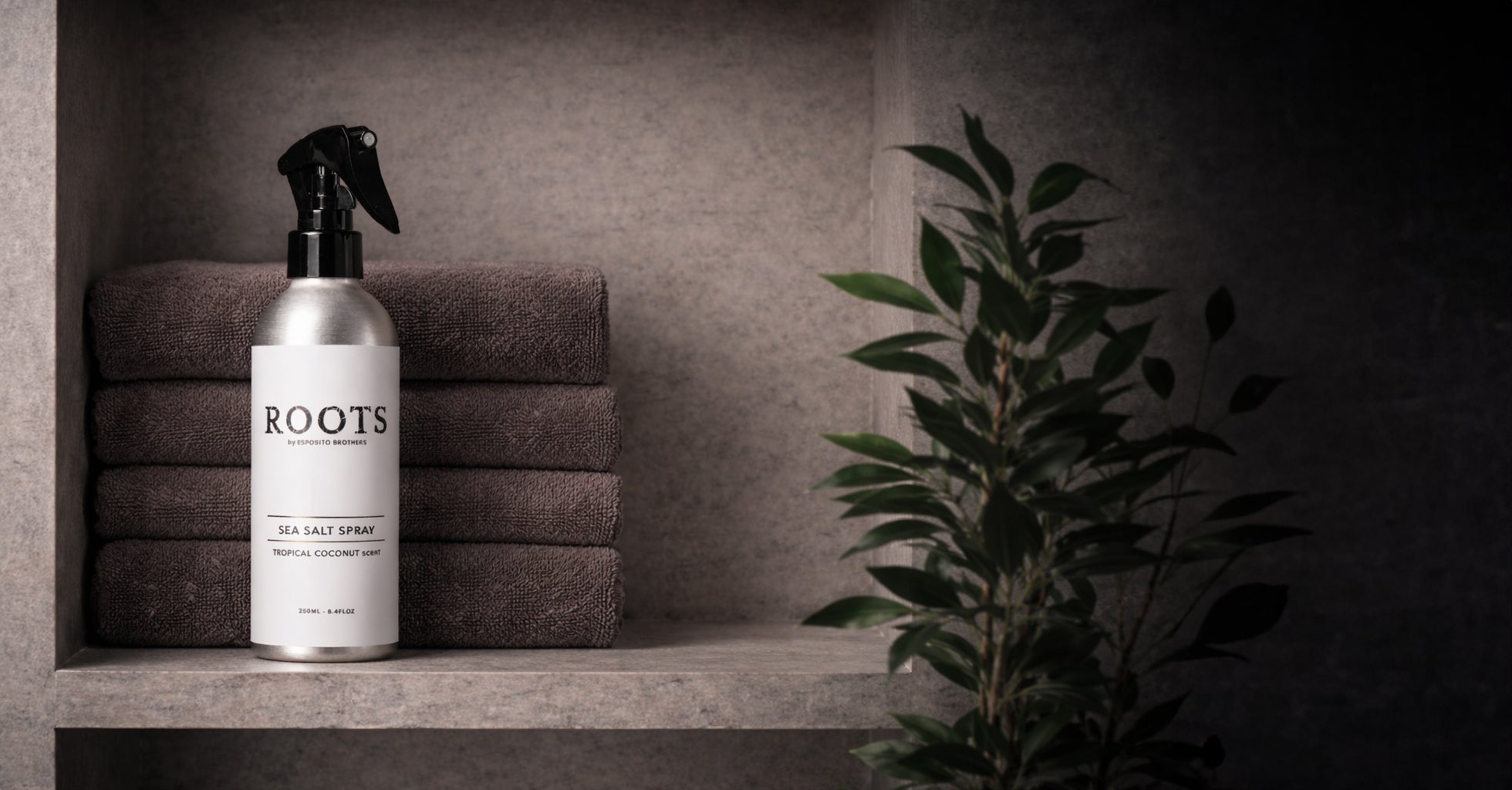 Bottle of 'ROOTS' sea salt spray on a shelf with towels and a plant in the background
